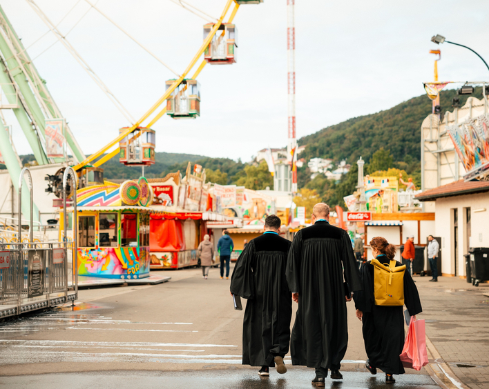 3 Pfarrer im Talar gehen über einen Rummelplatz
