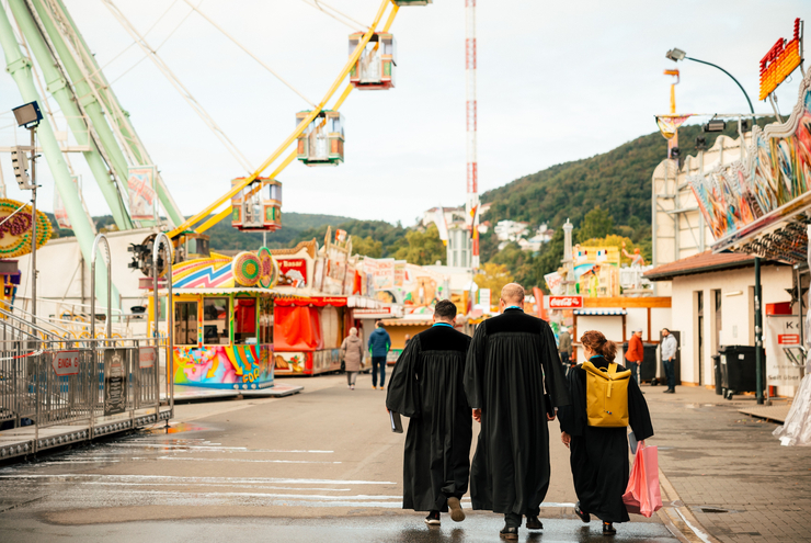 3 Pfarrer im Talar gehen über einen Rummelplatz