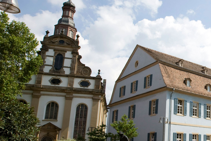 Barocke Stadtkirche mitten in Speyer: Die protestantische Dreifaltigkeitskirche. Im Vordergrund die Pilger-Statue. Foto: view
