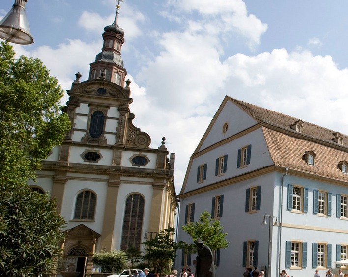 Barocke Stadtkirche mitten in Speyer: Die protestantische Dreifaltigkeitskirche. Im Vordergrund die Pilger-Statue. Foto: view