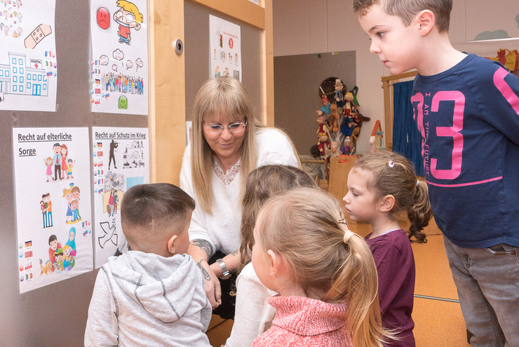Kinder und Kita-Leiterin Manuela Pascarella sprechen über Kinderrechte, die an einer Wand dargestellt sind. Foto: Prot. Kita-Verbund LU/Wagner  