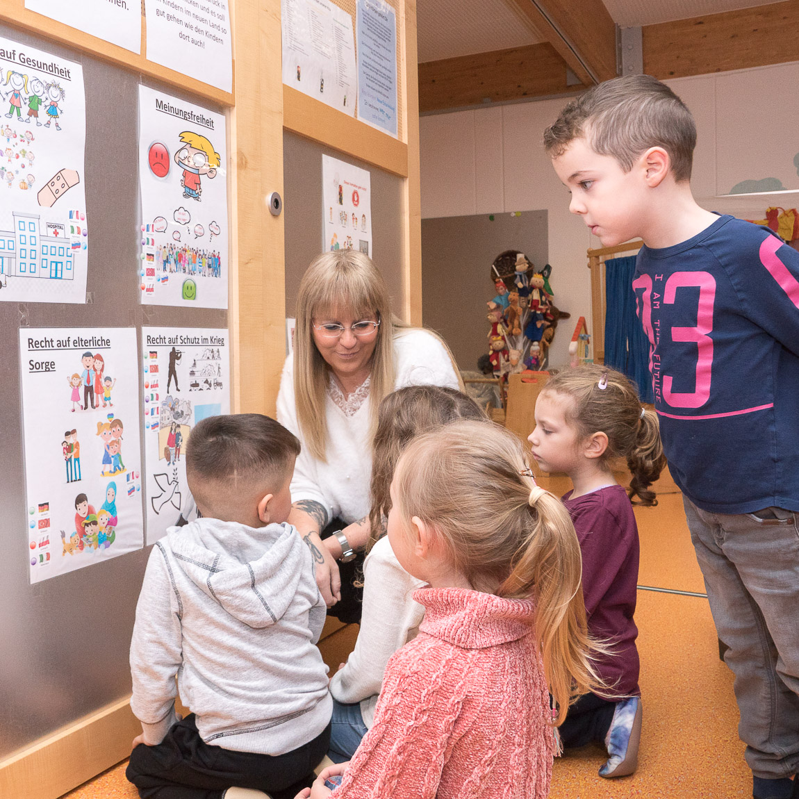 Kinder und Kita-Leiterin Manuela Pascarella sprechen über Kinderrechte, die an einer Wand dargestellt sind. Foto: Prot. Kita-Verbund LU/Wagner  