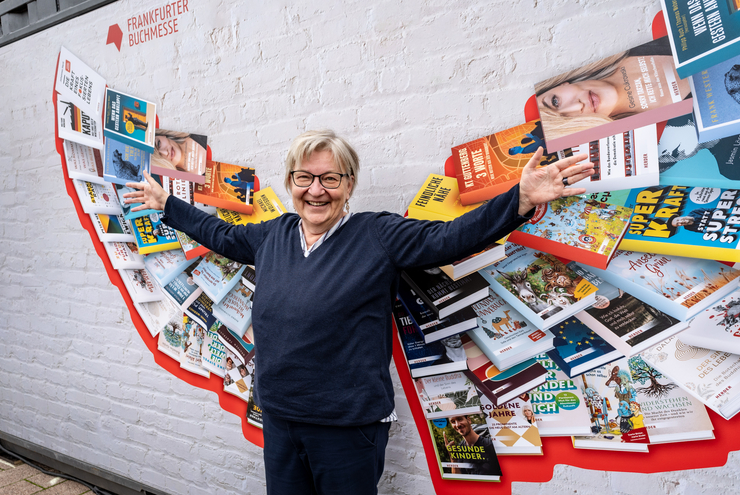 Ei9ne Frau steht vor einer Bücherwand. Dich Büchersind so angeordnet, dass sie wie Engelsflügel erscheinen. 