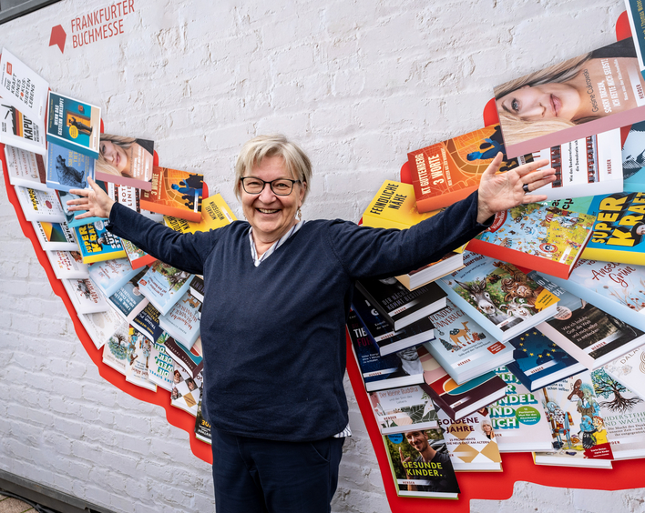Ei9ne Frau steht vor einer Bücherwand. Dich Büchersind so angeordnet, dass sie wie Engelsflügel erscheinen. 