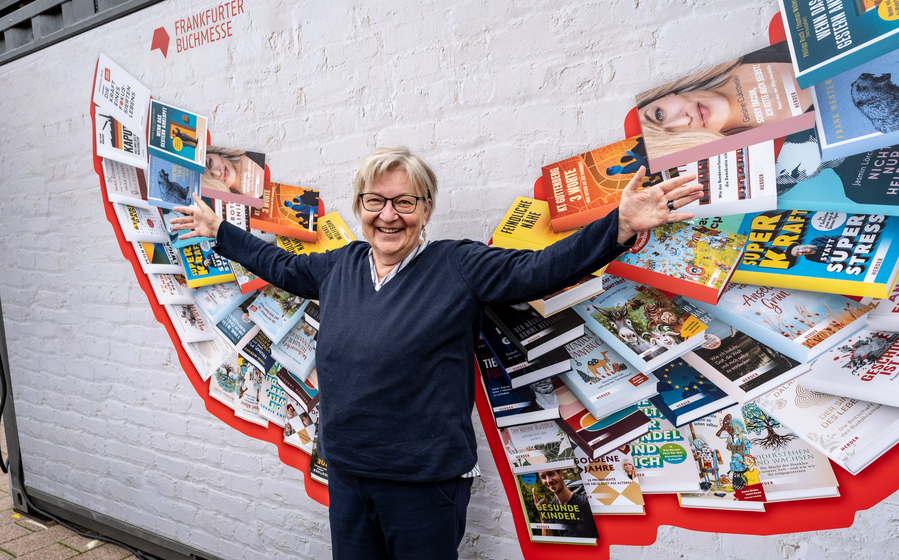 Ei9ne Frau steht vor einer Bücherwand. Dich Büchersind so angeordnet, dass sie wie Engelsflügel erscheinen.