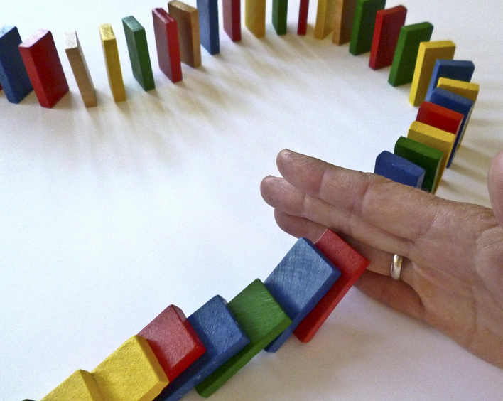 Eine Reihe Dominosteine wird durch eine Hand unterbrochen