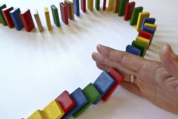 Eine Reihe Dominosteine wird durch eine Hand unterbrochen