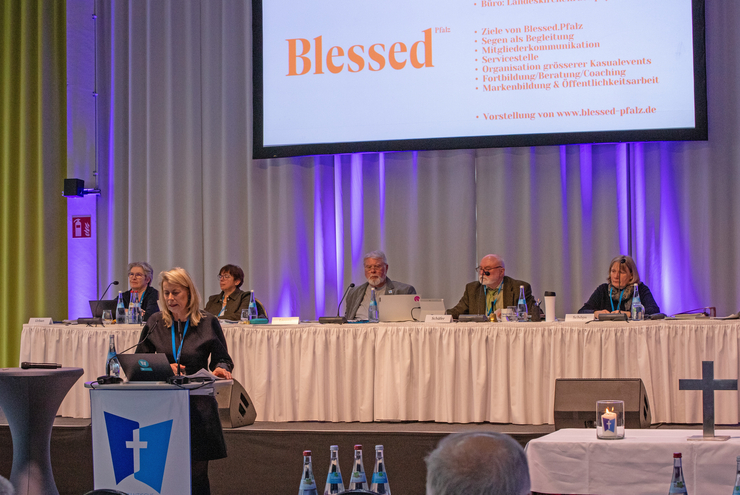 Eine Frau hält einen Vortrag. Im Hintergrund ist eine Leinwand mit der Präsentation zu sehen.