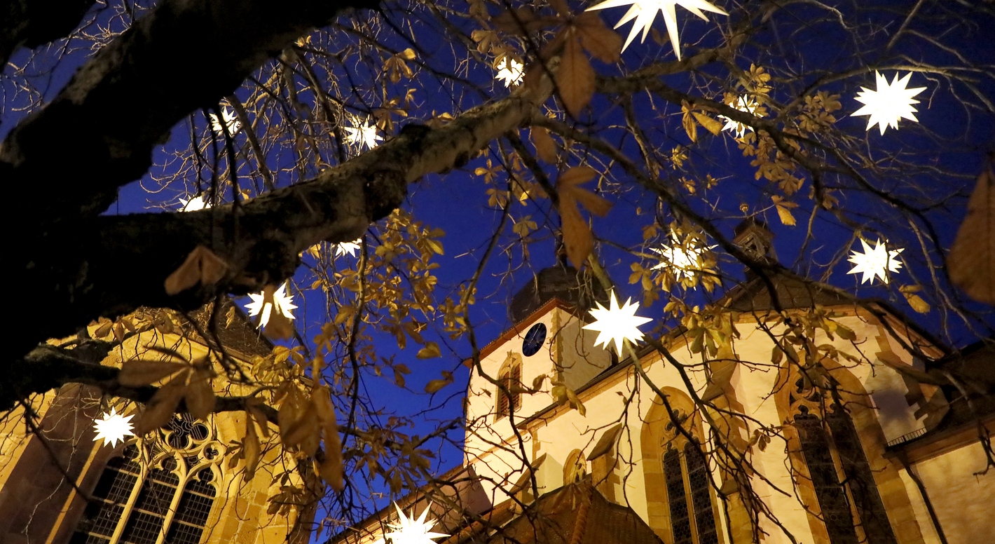 Blick durch beleuchtete Weihnachtssterne zu den Türmen der Protestantischen Kirche in Wachenheim.